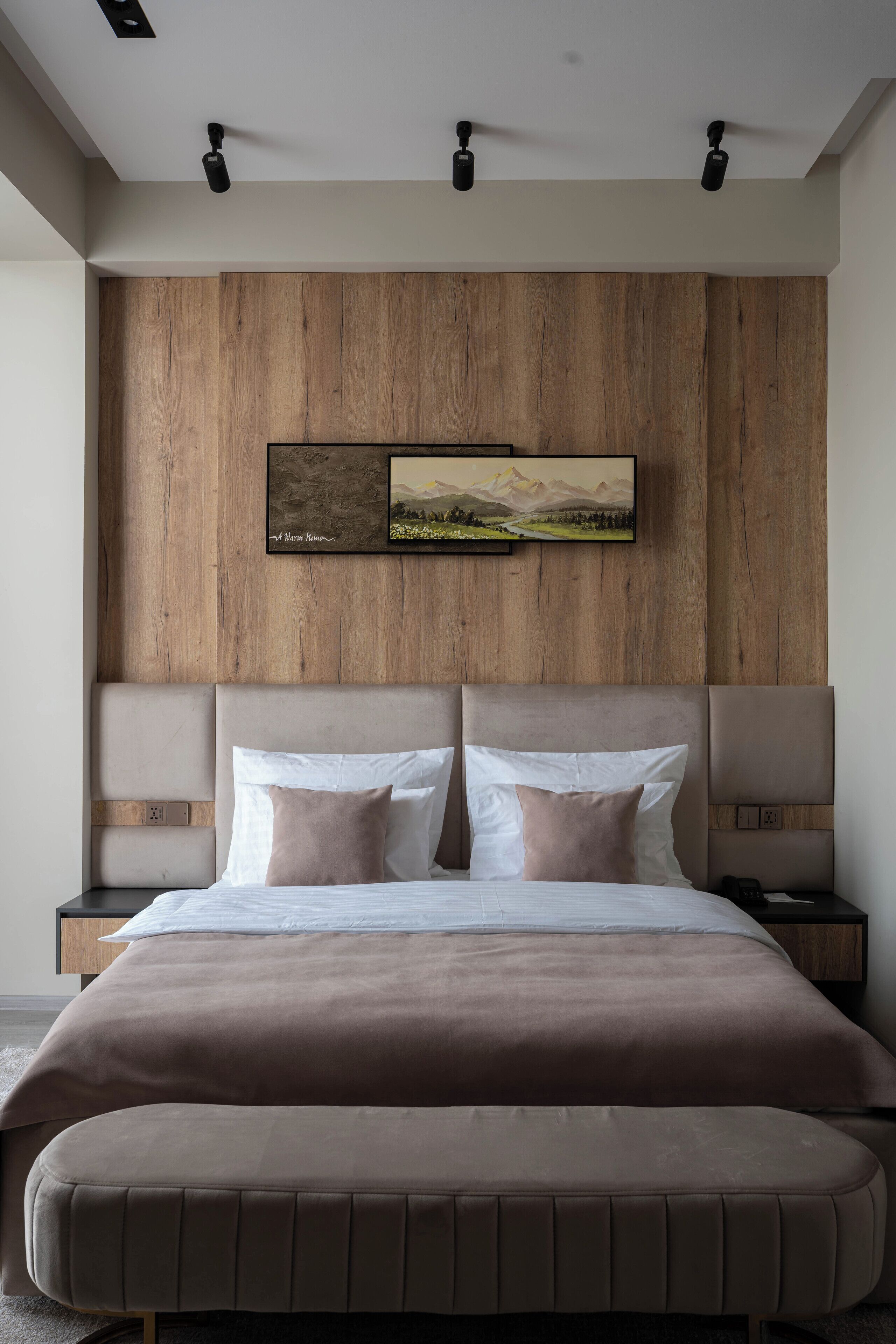 A modern bedroom with a wooden headboard, a large bed with two pillows, bedside tables, and a mounted artwork.