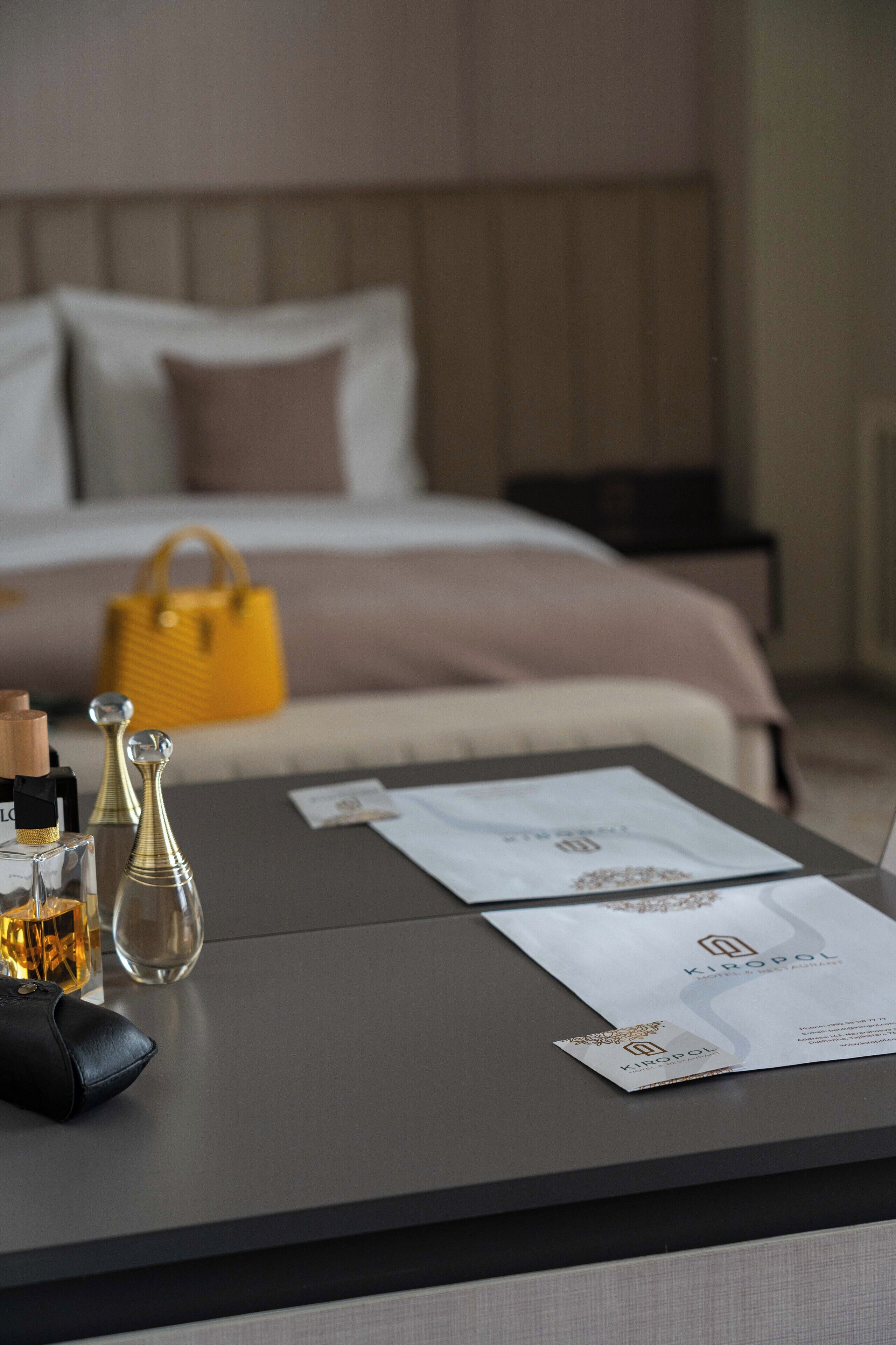 Une chambre d’hôtel bien rangée, avec un lit, une table de chevet sur laquelle sont posés des articles de toilette et un sac à main jaune.