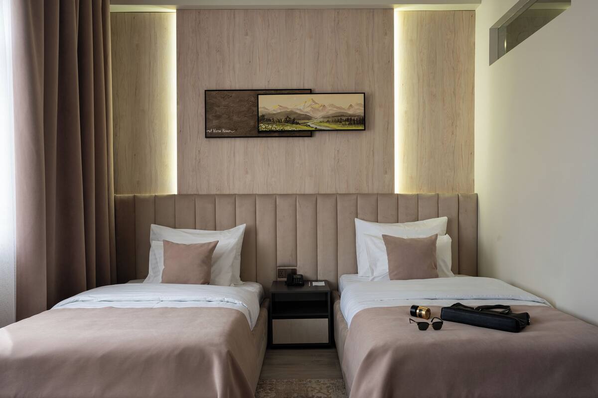 Ein Hotelzimmer mit zwei Betten, einem Nachttisch, einem Bild und einem Fenster mit Vorhängen.
