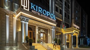 L’entrée d’un hôtel, avec un grand escalier, des colonnes et une enseigne indiquant « Kiropol Hôtel et Restaurant ».