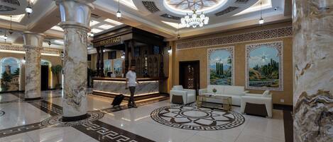 A lobby with marble columns, a reception desk, and a chandelier.