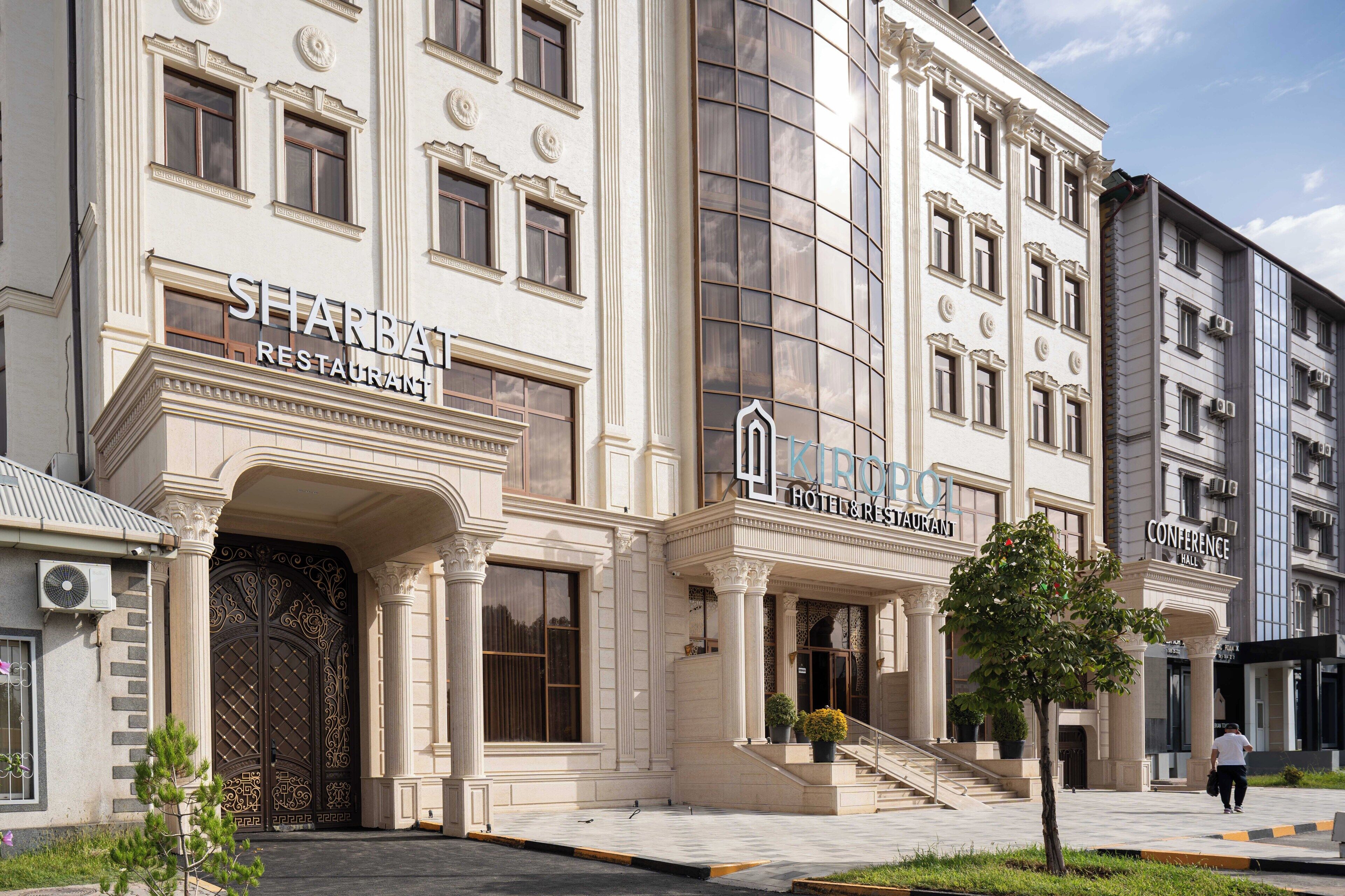 Ein Gebäude im klassischen Stil mit einem großen Eingang, der schmiedeeiserne Elemente, Säulen und ein Schild für 'SHARBA HOTEL RESTAURANT' zeigt.