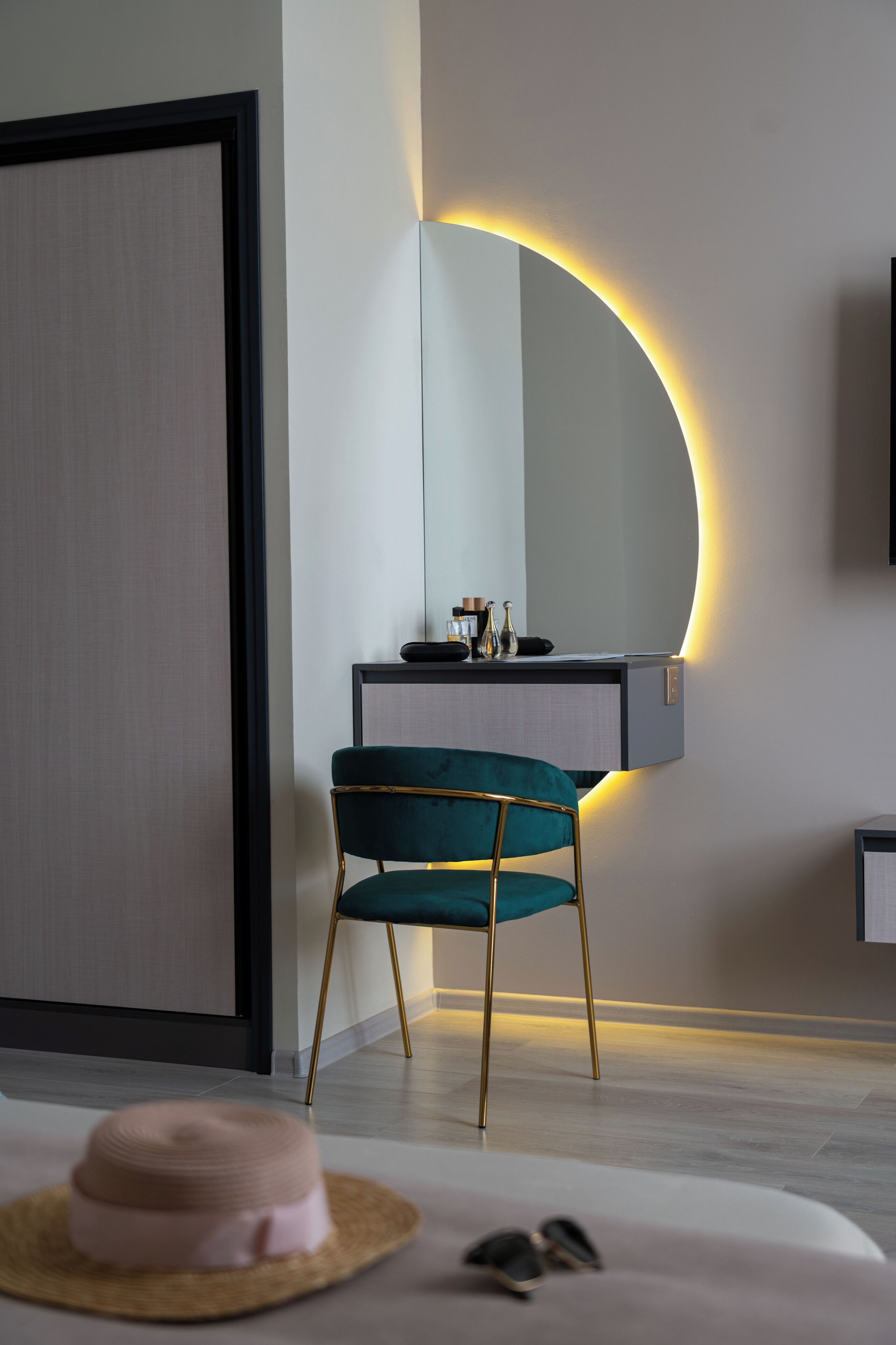 Een moderne kamer met een smaragdgroene fauteuil, een bureau met spiegel en een nachtkastje met hoed en zonnebril.