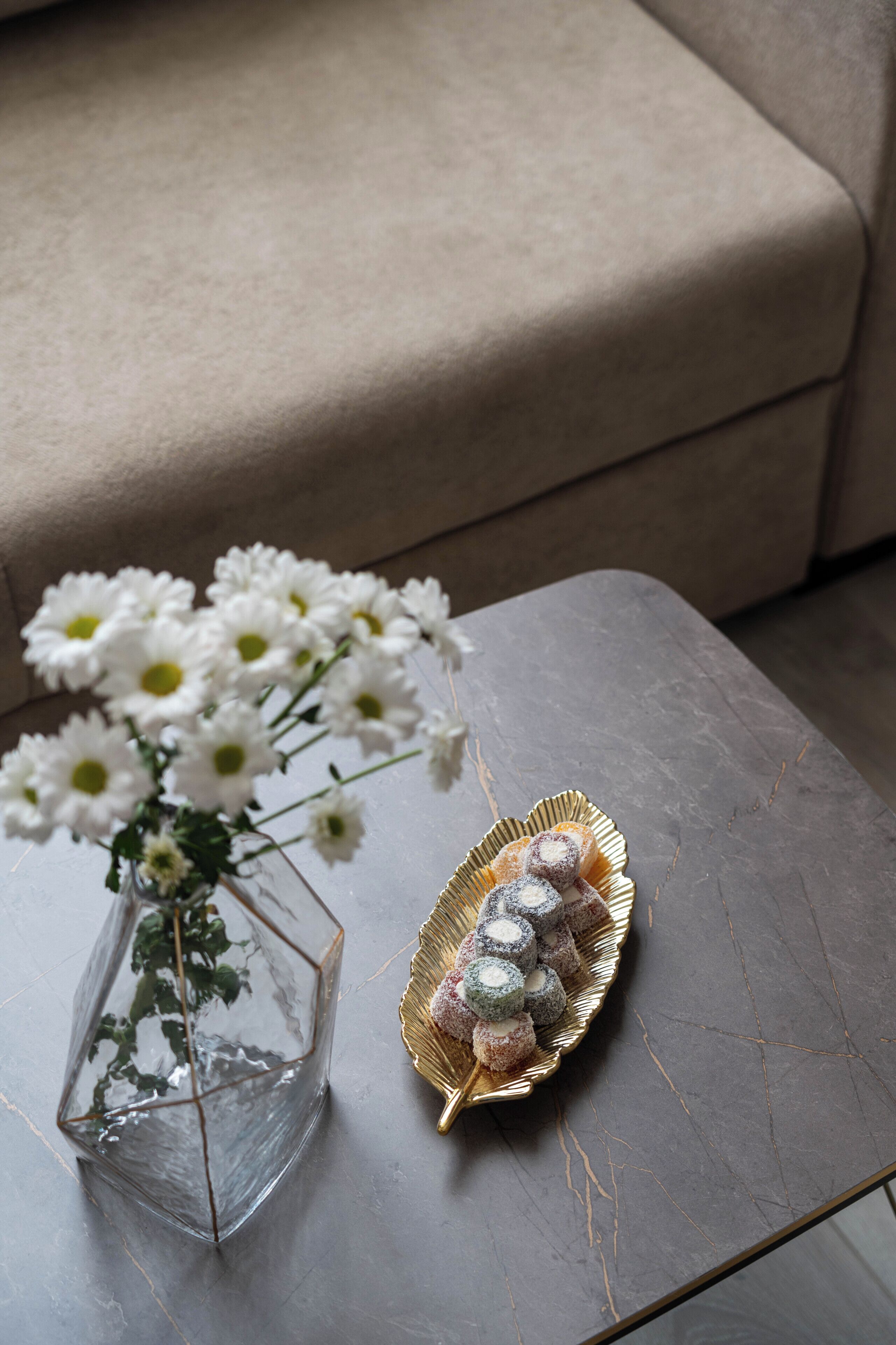 En genomskinlig glasvas med vita blommor står på ett marmorbord bredvid en kudde.
