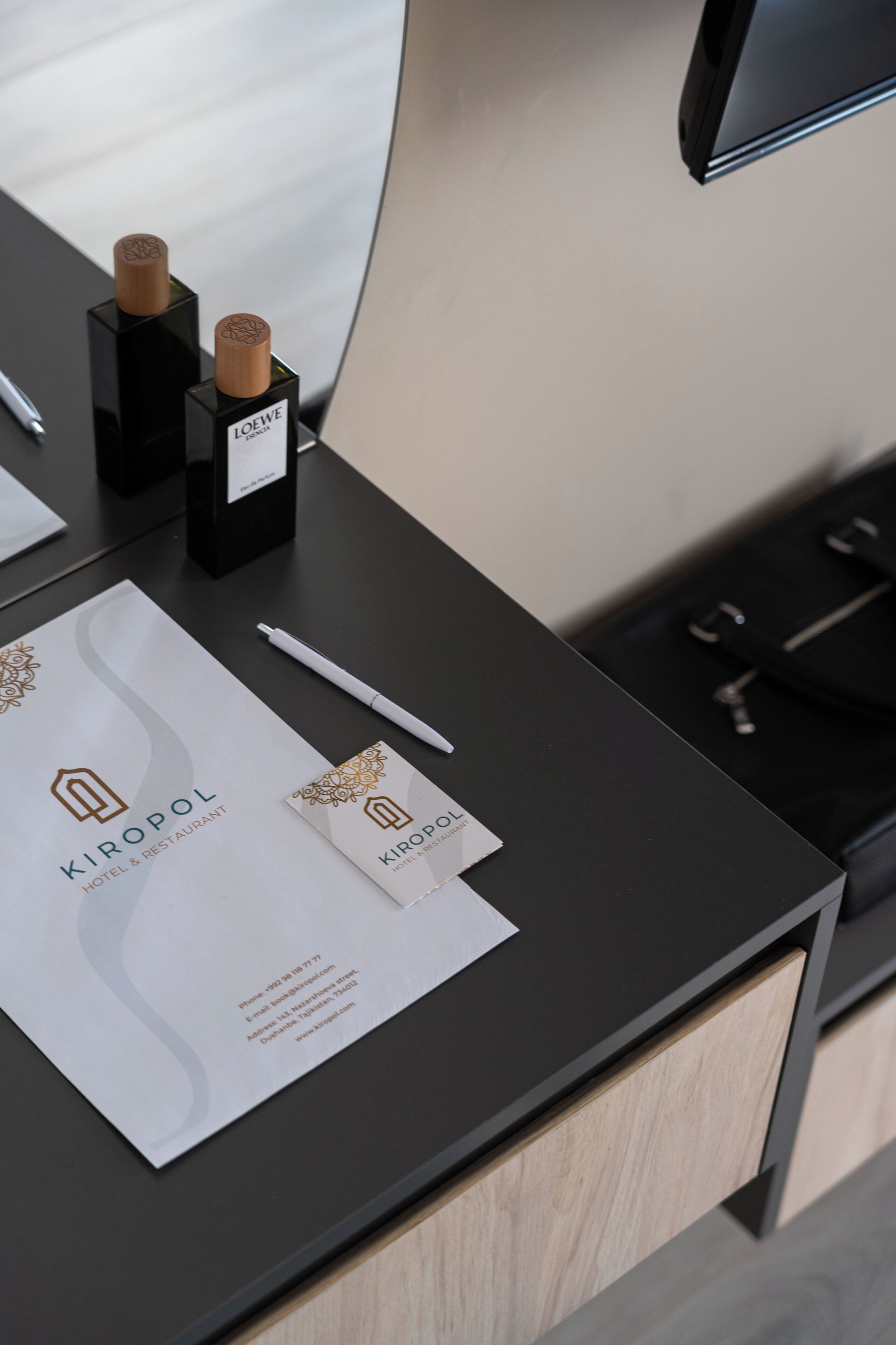 A hotel reception desk with a black counter, a white pen, two corks in black boxes, and a business card.