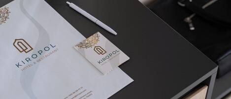 Un comptoir d’accueil d’hôtel avec un plan de travail noir, un stylo blanc, deux bouchons de liège dans des boîtes noires et une carte de visite.