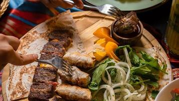 En måltid bestående av grillat kött, tunnbröd och sallad, serverad på en träbricka.