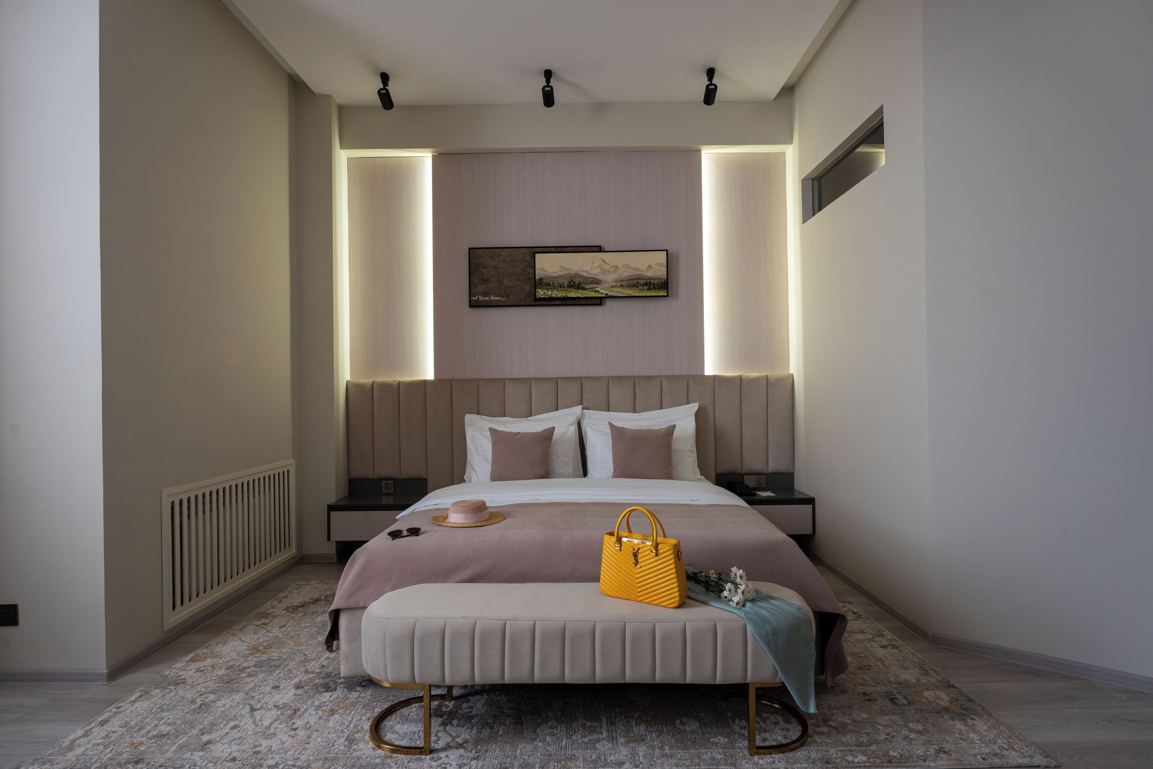 A modern bedroom with a large bed, bedside tables, a headboard with integrated lighting, and a framed landscape picture on the wall.