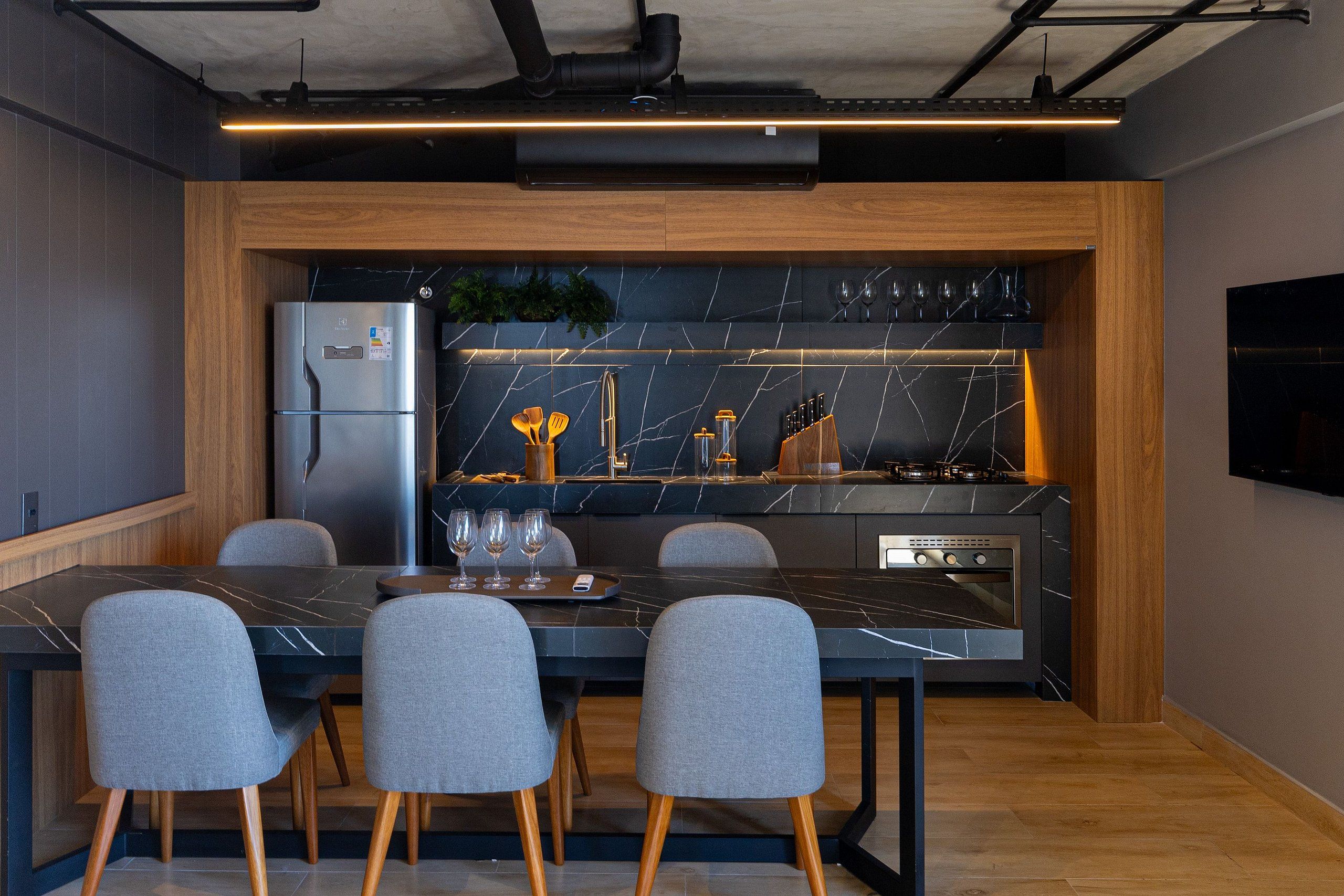 Une cuisine moderne équipée d’une cuisinière intégrée, d’un réfrigérateur et d’un coin repas avec un plan de travail en marbre et quatre chaises.