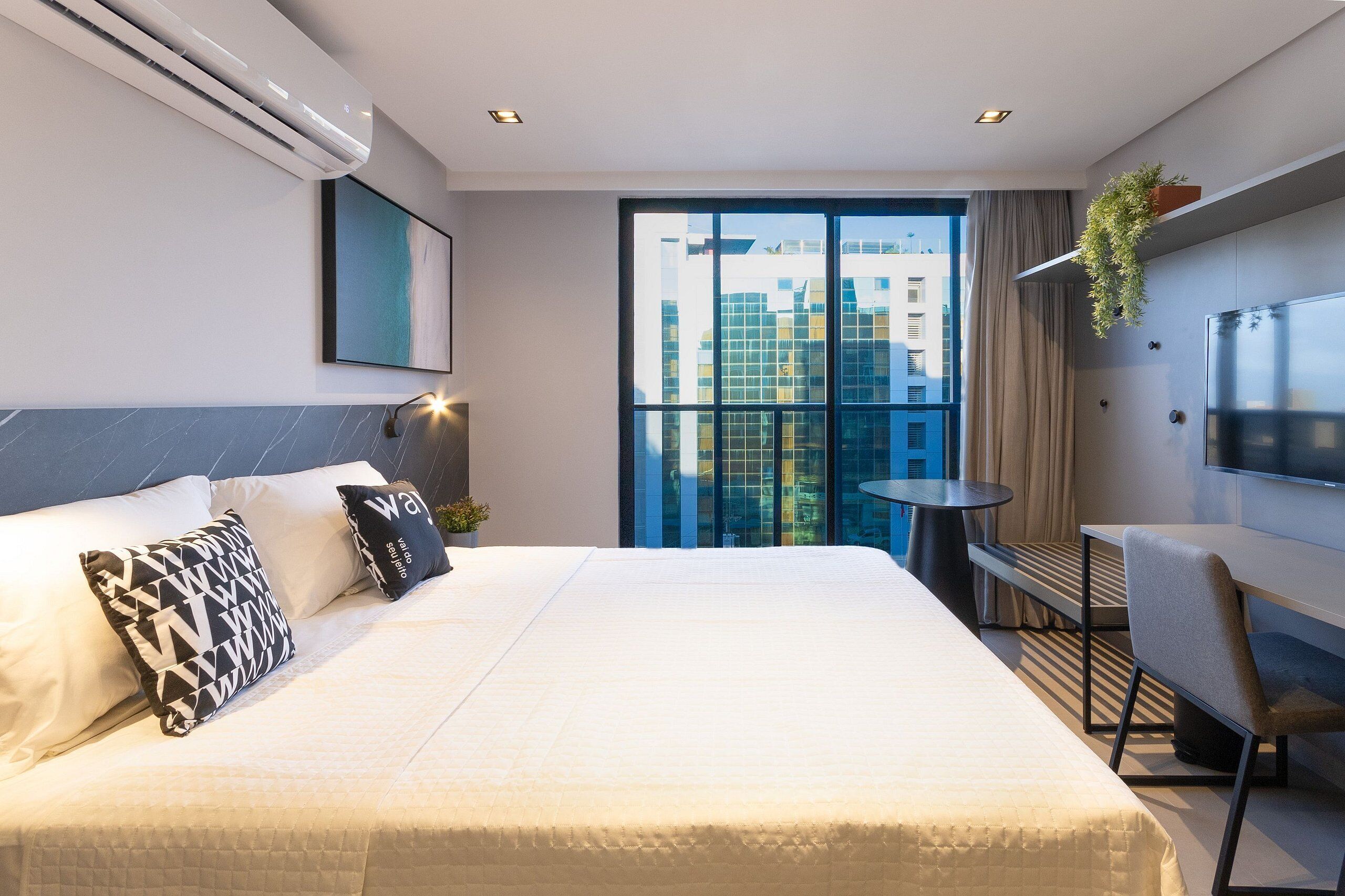 Quarto de hotel moderno com uma cama grande, uma escrivaninha e uma televisão.