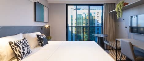 Quarto de hotel moderno com uma cama grande, uma escrivaninha e uma televisão.