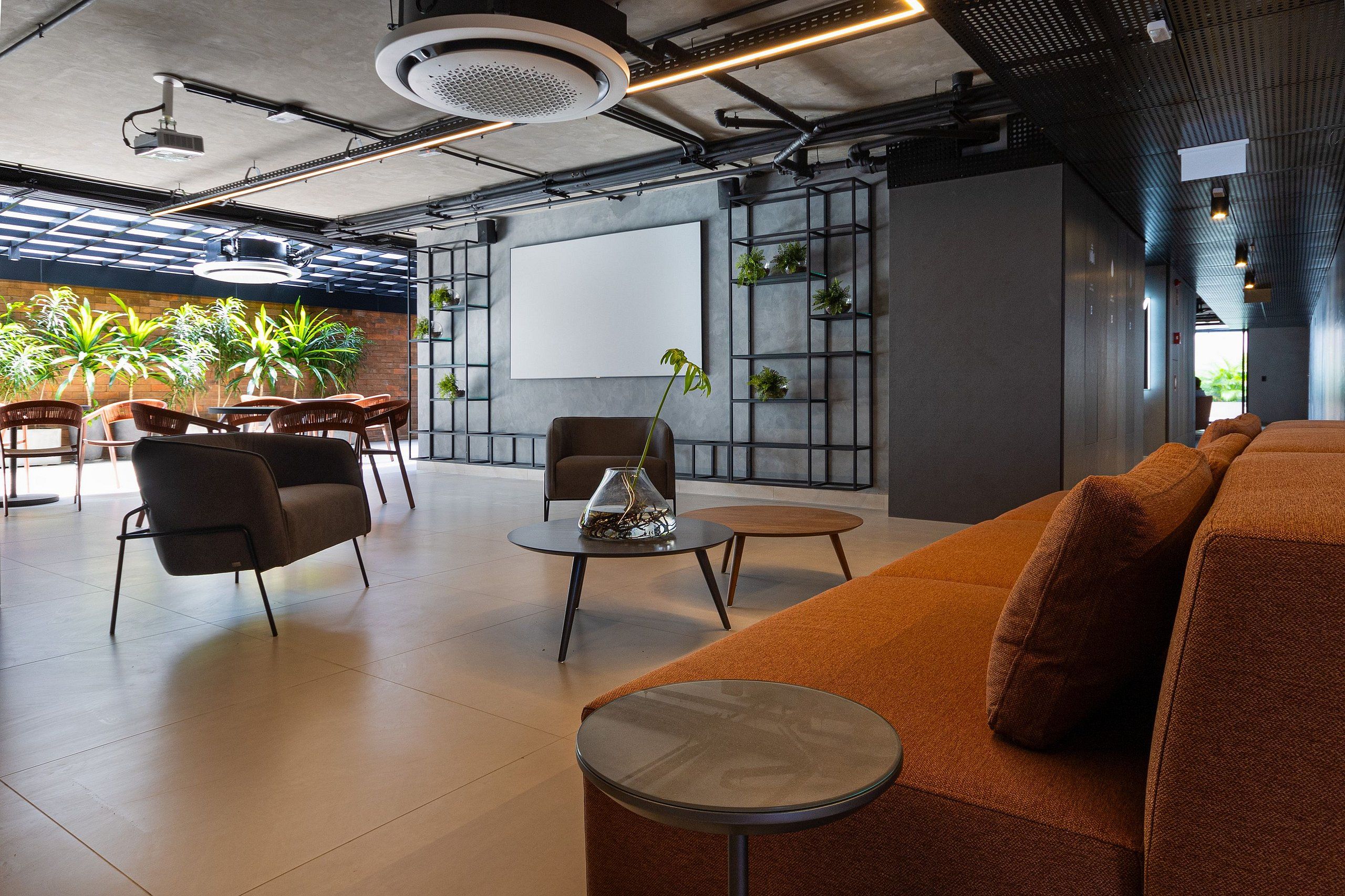 Un espacio lounge moderno con asientos, pantalla de proyector y plantas de interior.