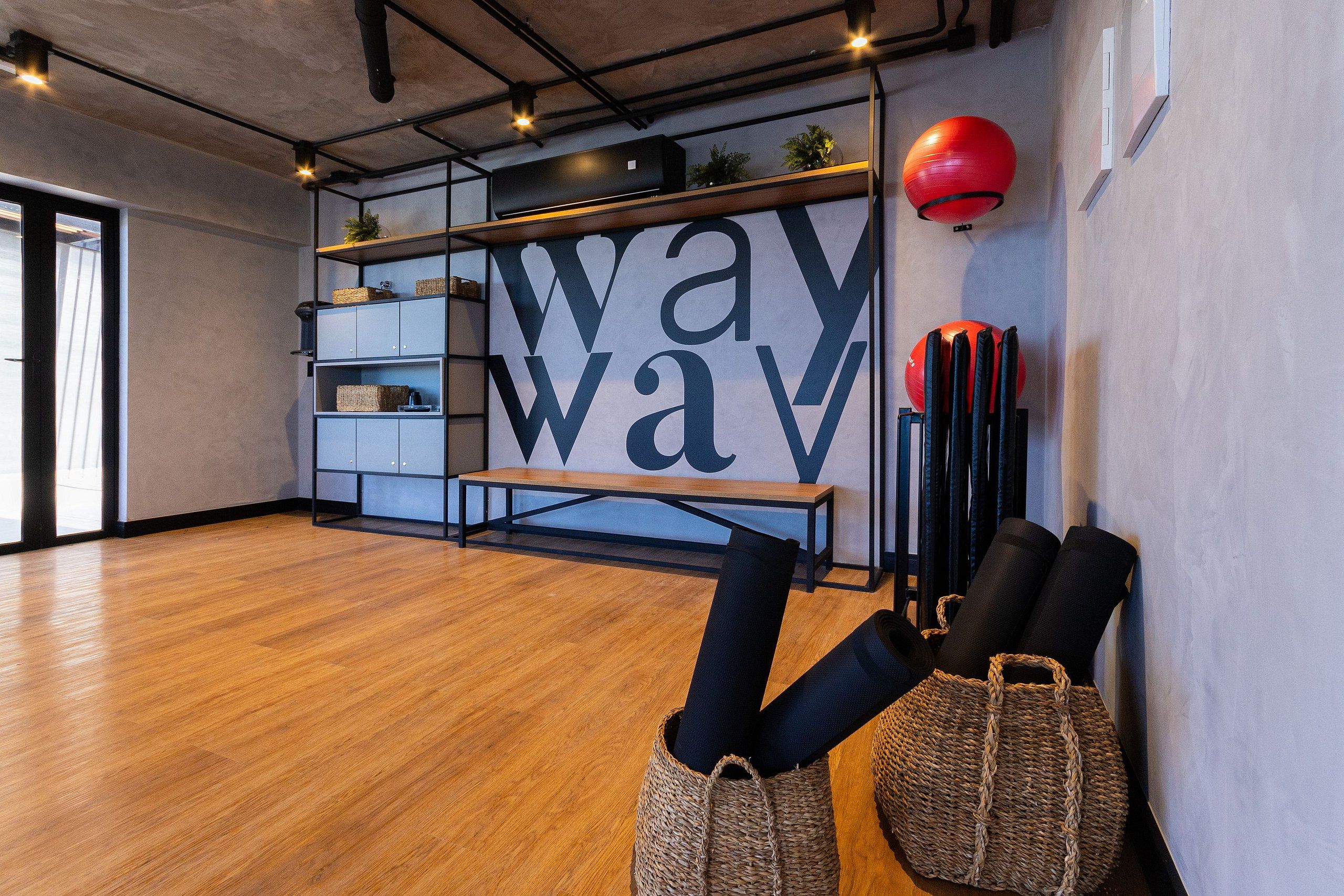 A modern room with a wooden floor, a large wall-mounted shelf with baskets, a bench, and exercise equipment.