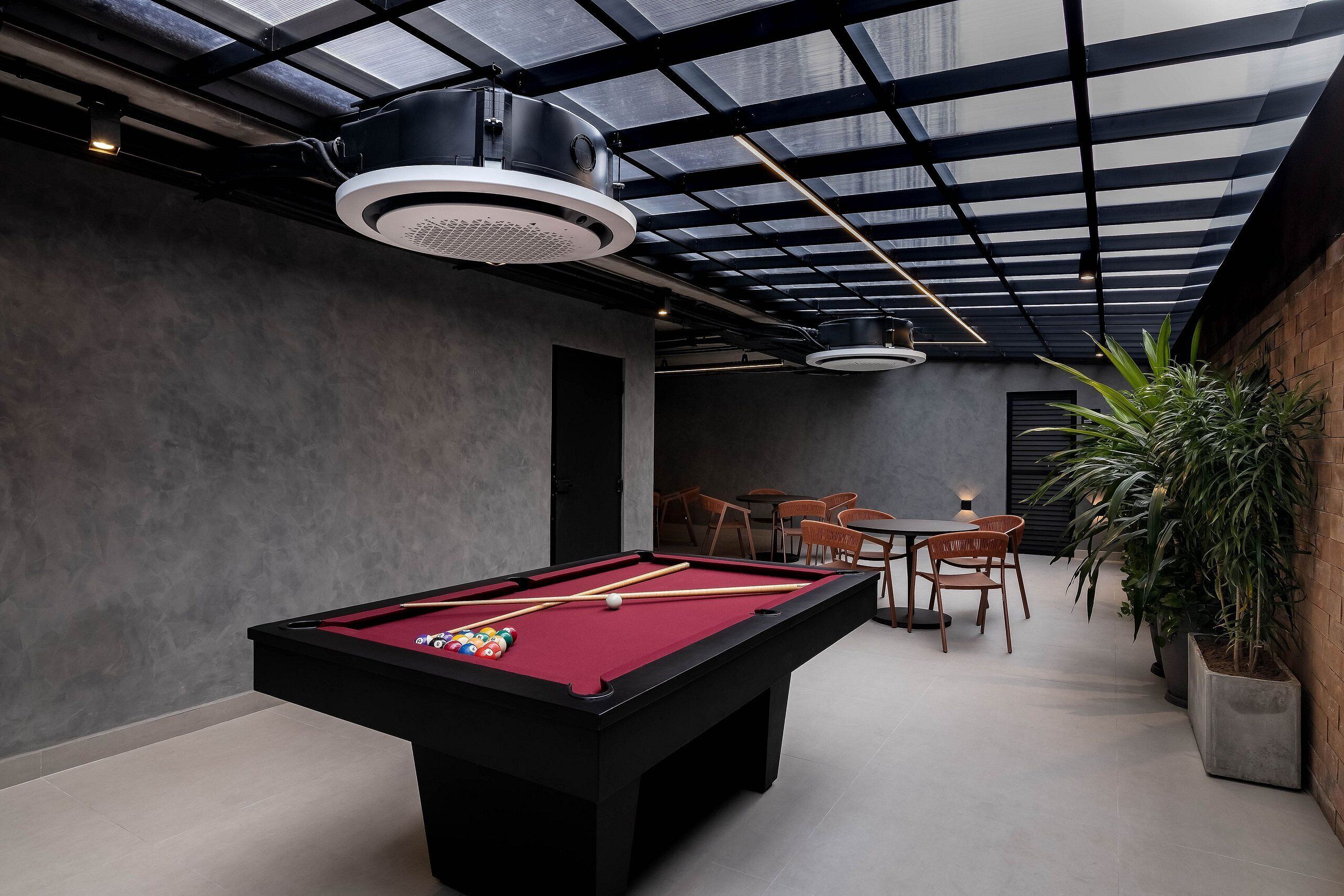 A pool table with pool cues and balls, a dining area with chairs, and a large potted plant.