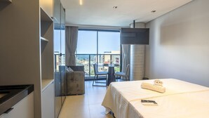 A hotel room with a bed, a desk, a chair, a TV, and a balcony with a view of the city. - Way Tambaú - João Pessoa by Carpediem (João Pessoa)