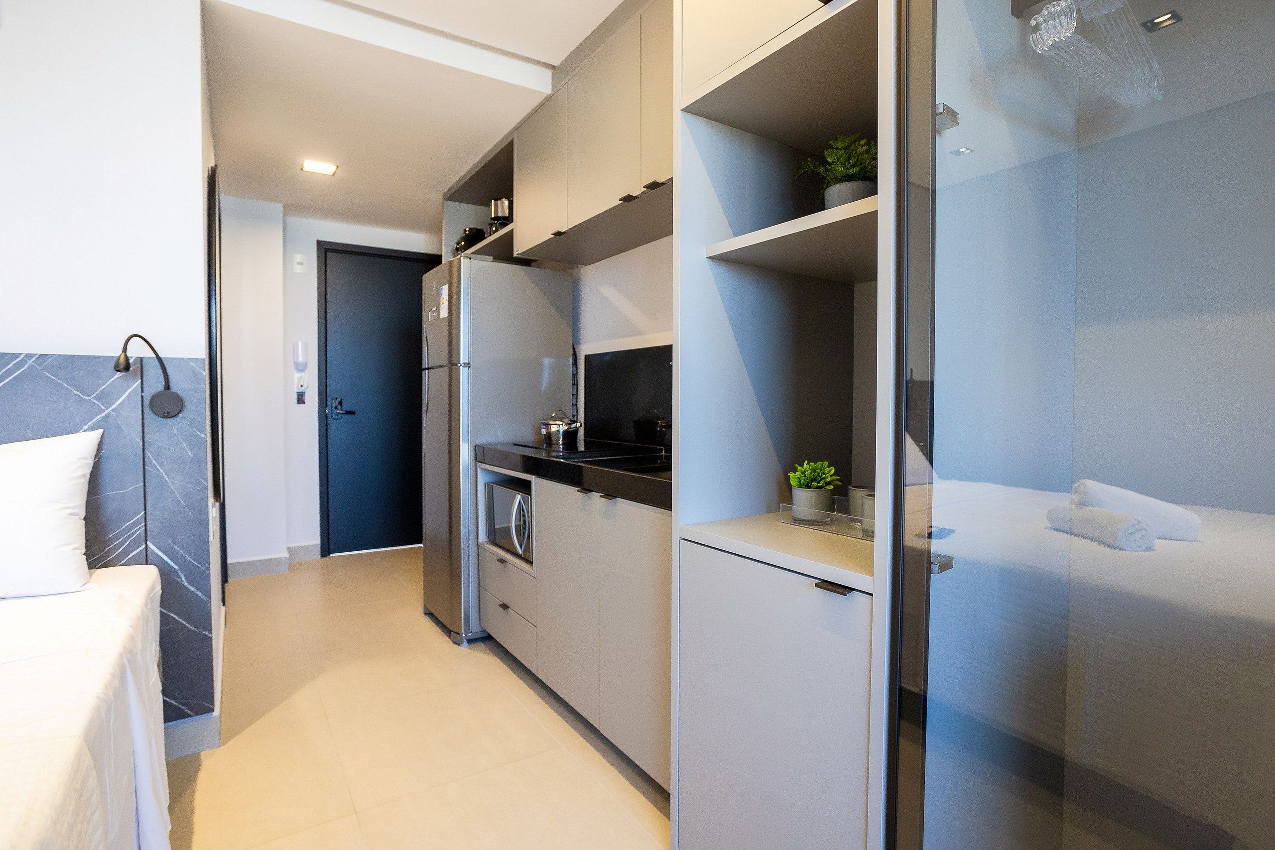 Una habitación de hotel moderna con kitchenette, cama y baño con cabina de ducha de vidrio.