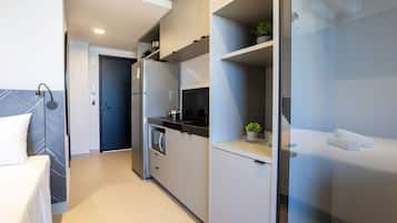 A modern hotel room with a kitchenette, a bed, and a bathroom with a glass shower enclosure.