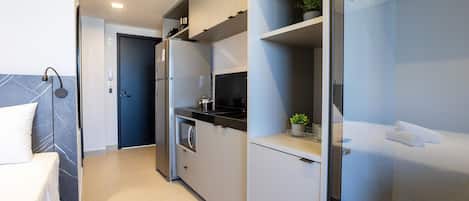 Quarto de hotel moderno com cozinha compacta, uma cama e banheiro com chuveiro de vidro.