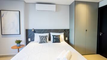 Una habitación de hotel moderna con una cama grande, una mesita de noche con una planta y un armario negro.