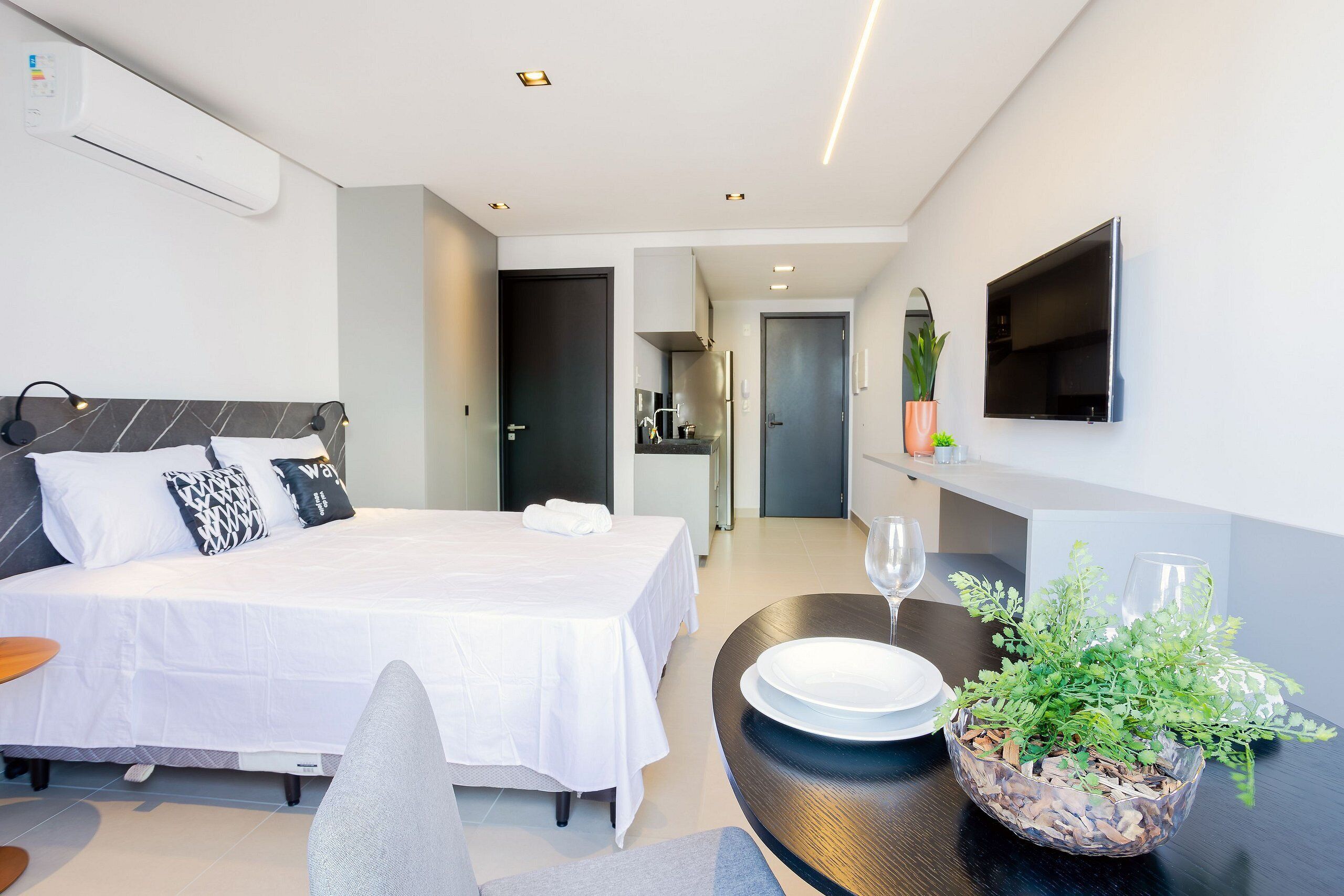 A modern hotel room with a neatly made bed, a dining table with plates and a glass, and a potted plant.