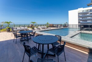 Area piscina sul tetto con poltrone relax, un tavolo rotondo e vista sull'oceano.