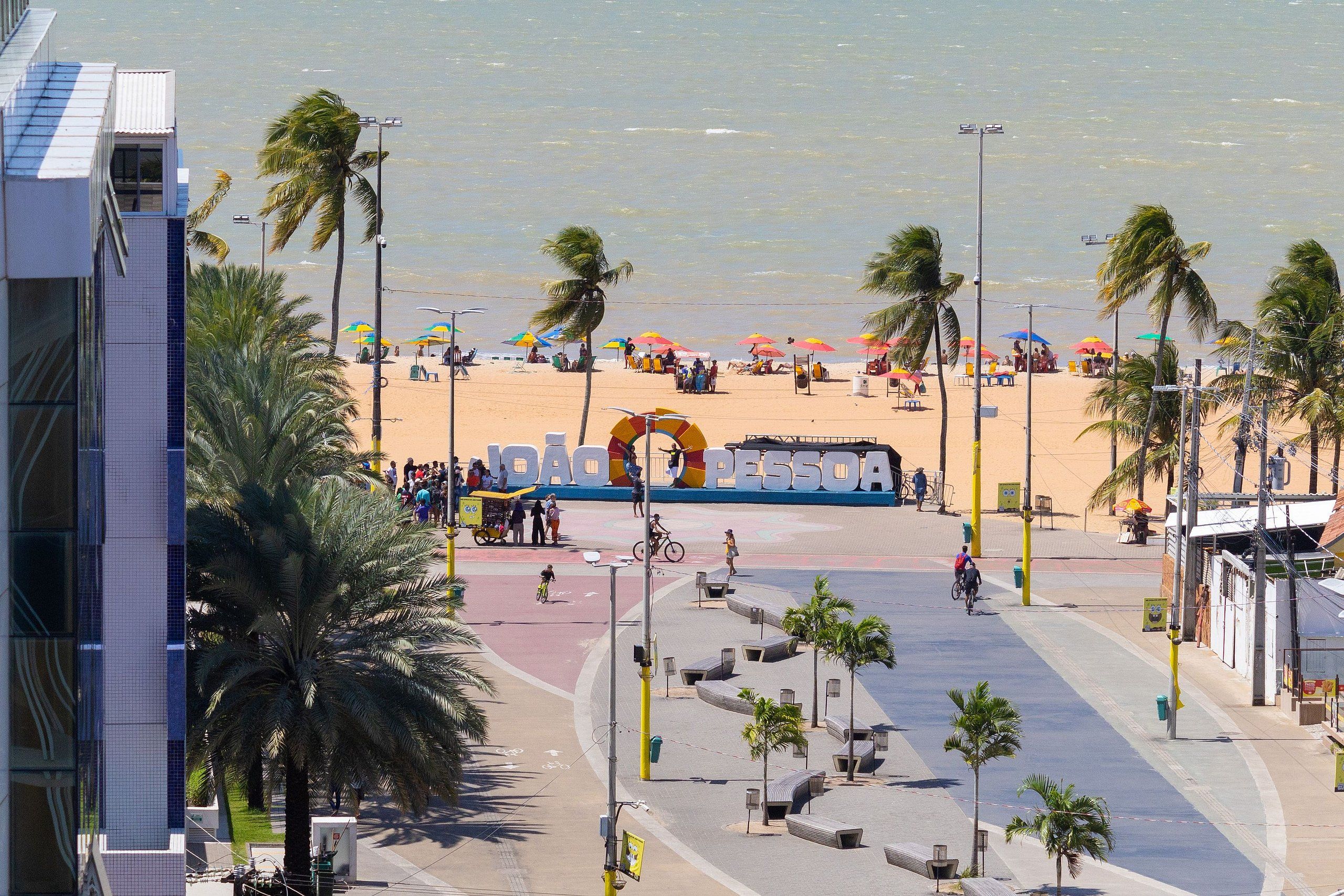 A beach with palm trees, umbrellas, and a sign reading "LOBO PESSOA".