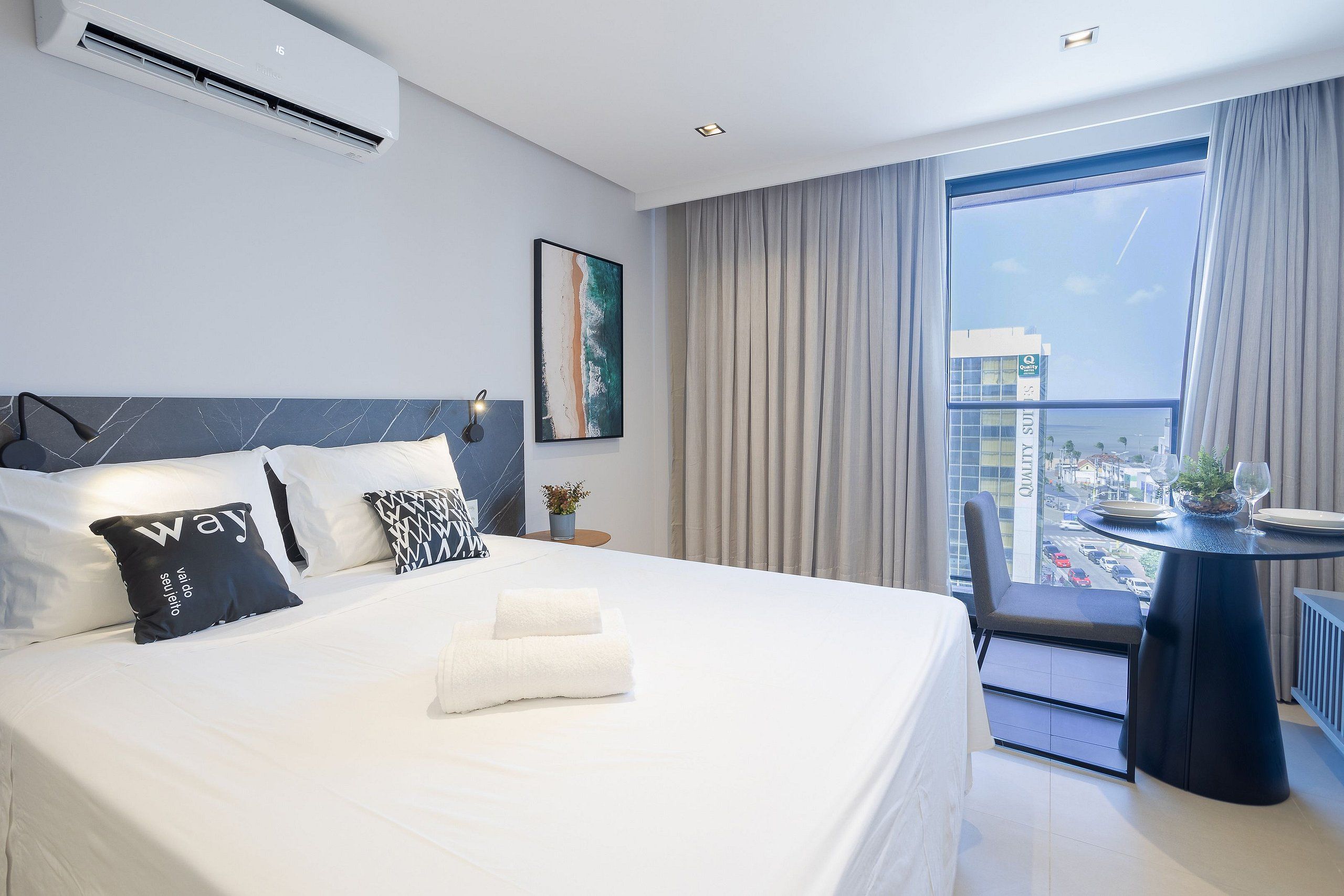 A modern hotel room with a large bed, a small table, and a view of the city.