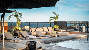 A rooftop pool area with lounge chairs, a small table, and a large umbrella. - Way Tambaú - João Pessoa by Carpediem (João Pessoa)