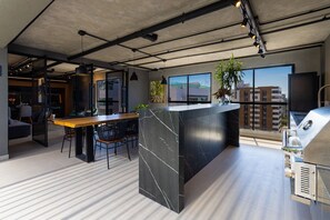 A modern kitchen with a marble island, a dining area, and a large window with a city view. - Way Tambaú - João Pessoa by Carpediem (João Pessoa)