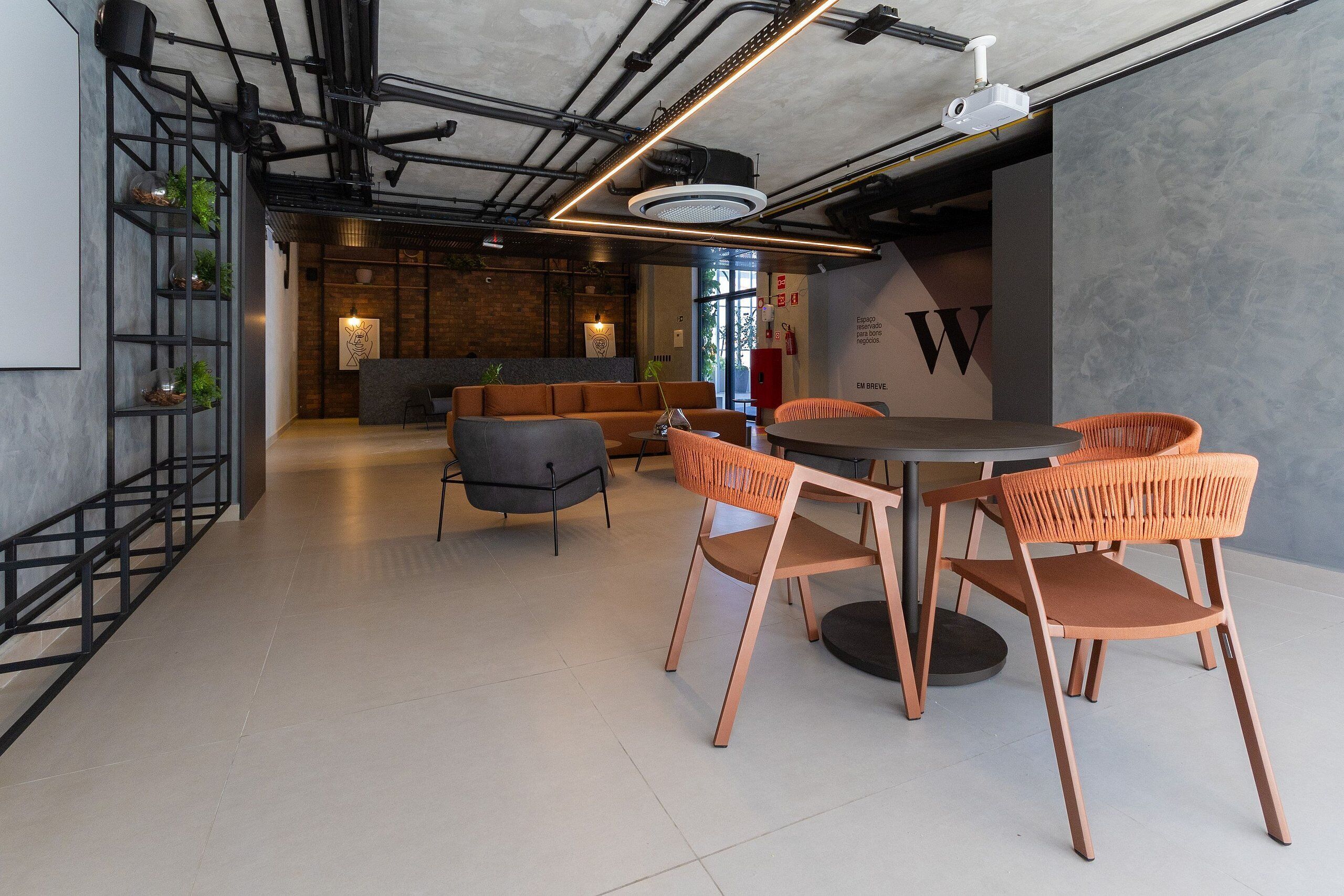 Ein modernes Interieur mit freiliegenden Rohren, einem runden Tisch mit orangefarbenen Stühlen und einer Ziegelwand mit einem großen 'W'-Schild.