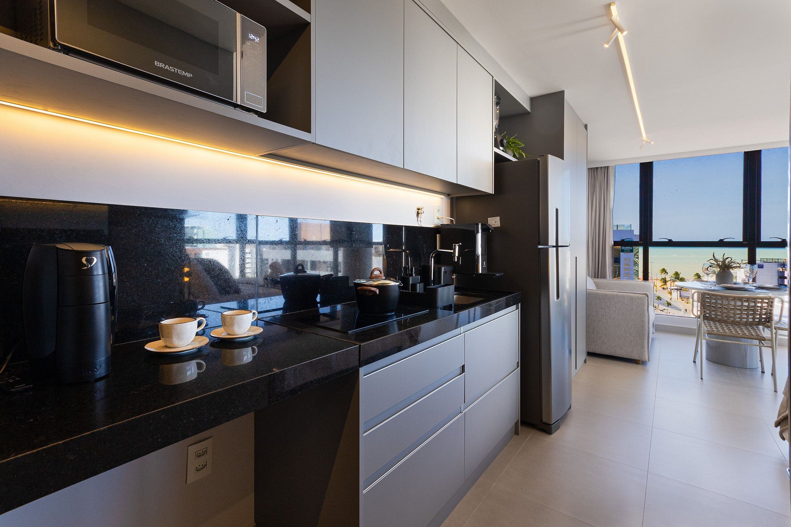 Una cocina moderna con encimera negra, electrodomésticos de acero inoxidable y vistas a la ciudad a través de amplios ventanales.
