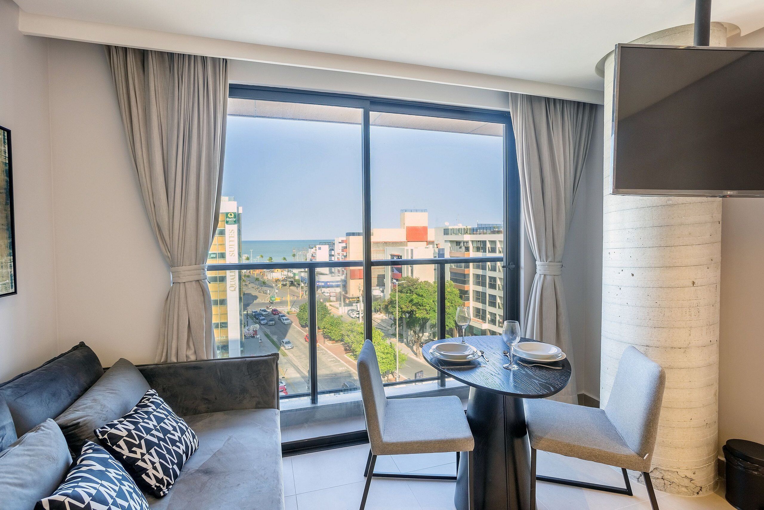 A modern living room with a sofa, a dining table with chairs, and a large window offering a city view.