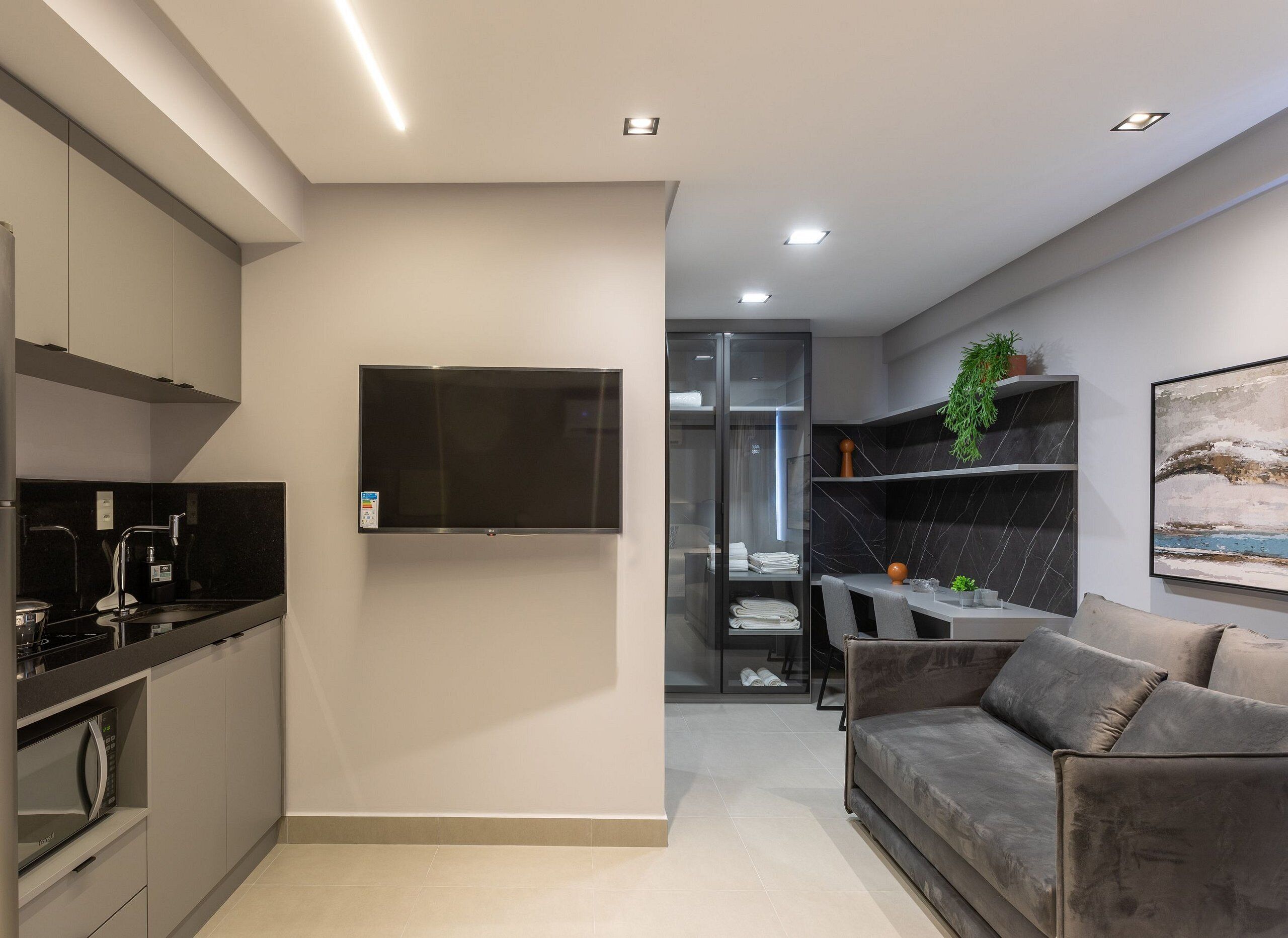 Eine moderne Küche mit Fernseher, ein Essbereich mit Tisch und Stühlen sowie ein graues Sofa im Wohnzimmer.