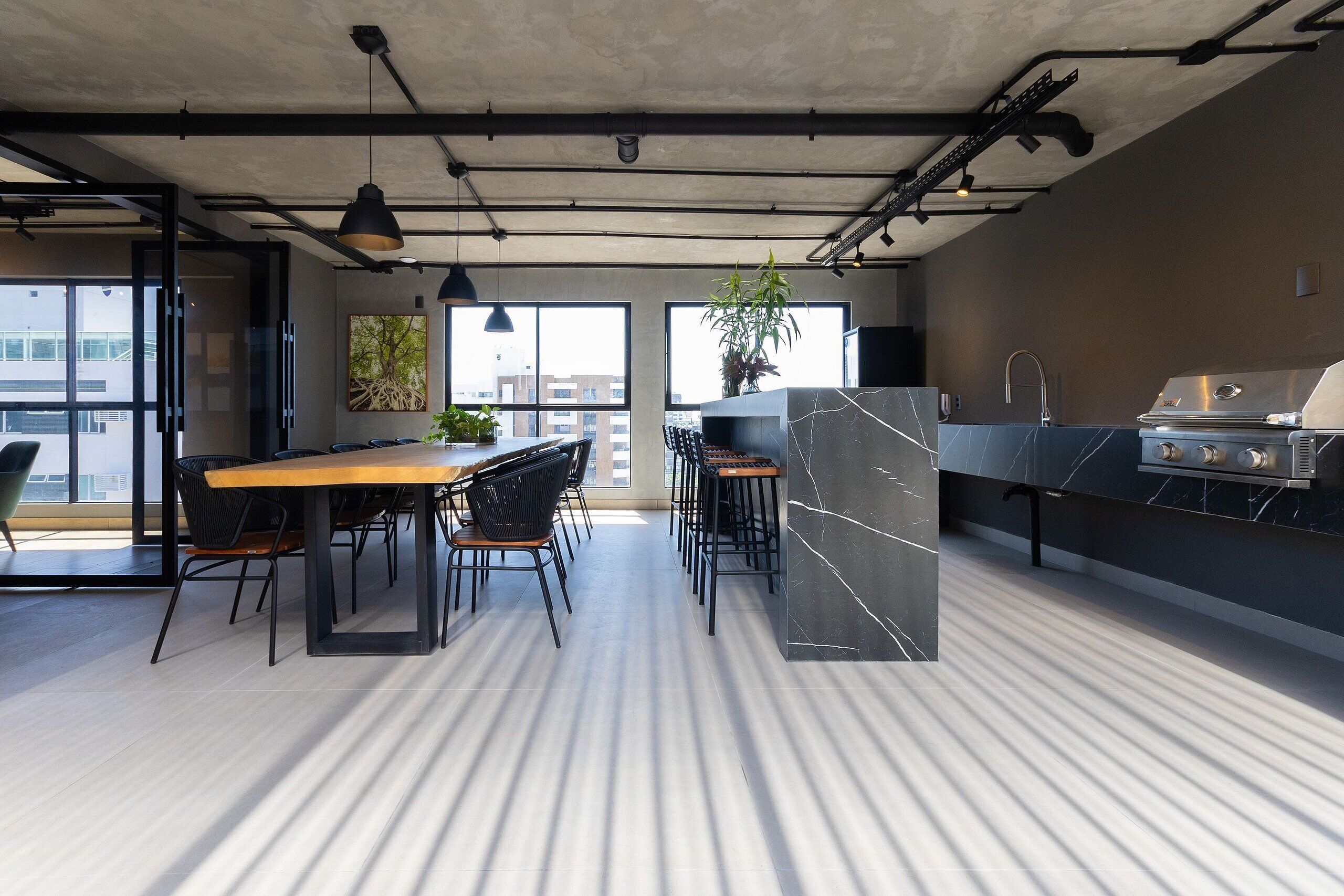 A modern kitchen with a built-in grill, large windows, and a dining area with a long table and chairs.