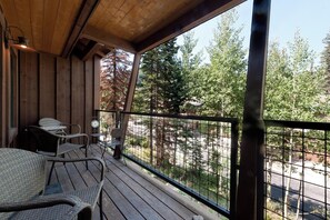 A wooden deck with wicker chairs and a metal table, overlooking a forested area.