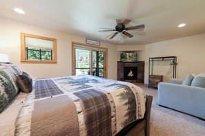 A bedroom with a large bed, a fireplace, a ceiling fan, and a view of the outdoors through a sliding door.