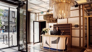 A reception area with a modern design, featuring a reception desk, a chandelier, and a view of the street outside. - The Diamond (Amsterdam)