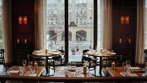 A restaurant with tables set for dining, candles on each table, and a view of a building through large windows. - The Diamond (Amsterdam)