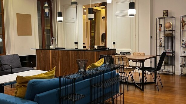 Un salon moderne avec un canapé bleu, un plancher en bois et des luminaires suspendus.