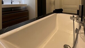 Une salle de bain moderne avec une grande baignoire, un meuble-lavabo avec un miroir et une porte donnant sur une autre pièce.