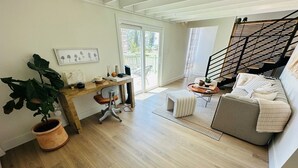 Una sala de estar moderna con piso de madera, un sofá gris, un escritorio de madera, una planta en maceta y una escalera.