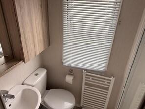A compact bathroom with a toilet, sink, and window blinds. - Cozy Coastal Caravan in Skegness (Skegness)