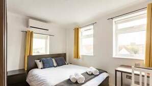 A hotel room with a bed, a desk, and two windows with curtains. - 4 Guests - 2 Bedrooms - Quick Links Central London (London)