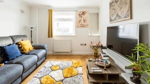 A living room with a grey sofa, yellow cushions, a modern TV, and a decorative rug. - 4 Guests - 2 Bedrooms - Quick Links Central London (London)