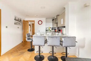 A modern kitchen with a dining area featuring a white table and four grey chairs. - 4 Guests - 2 Bedrooms - Quick Links Central London (London)