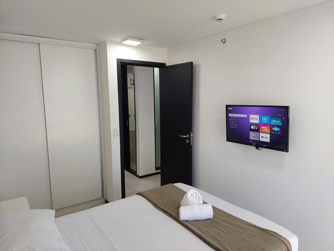 Una habitación de hotel con una cama, un televisor montado en la pared, una puerta y un espejo.
