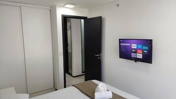 Una habitación de hotel con una cama, un televisor montado en la pared, una puerta y un espejo.