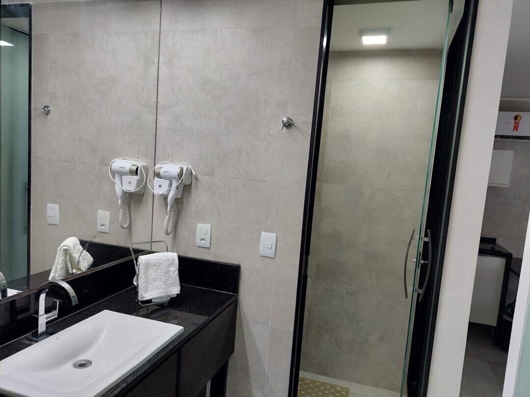 Un baño moderno con lavamanos de superficie negra, cabina de ducha de vidrio y dos secadores de pelo montados en la pared.