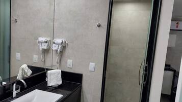 Un baño moderno con lavamanos de superficie negra, cabina de ducha de vidrio y dos secadores de pelo montados en la pared.