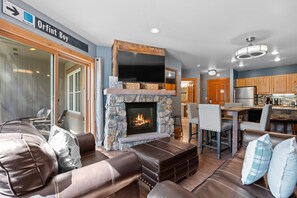 A modern living room with a stone fireplace, leather seating, and a flat-screen TV mounted above it. - Short Walk to Lifts & Village Amenities & Private Balcony Overlooks Pool! (Keystone)